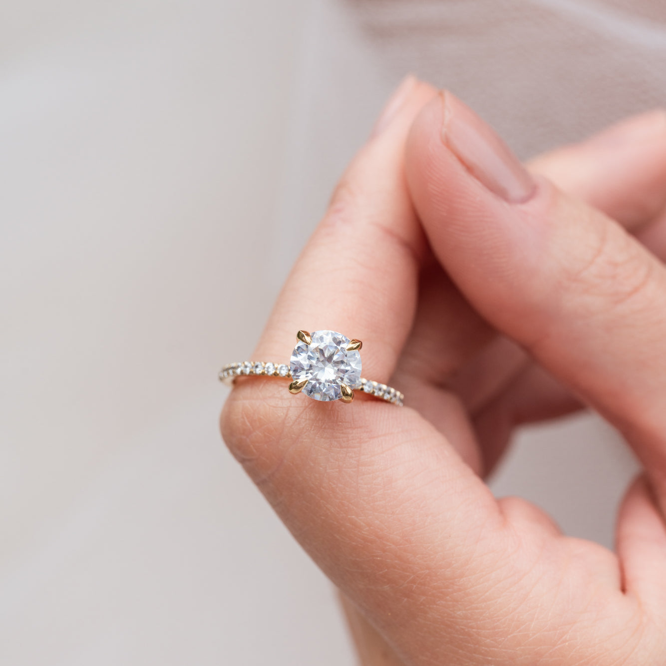 Rose - Micheli Jewellery. Yellow gold engagement ring with round brilliant cut diamond centre stone with 4 claw setting and diamond pave band modelled on hand. Engagement ring on hand. Yellow gold engagement ring on hand. Diamond pave engagement ring on hand