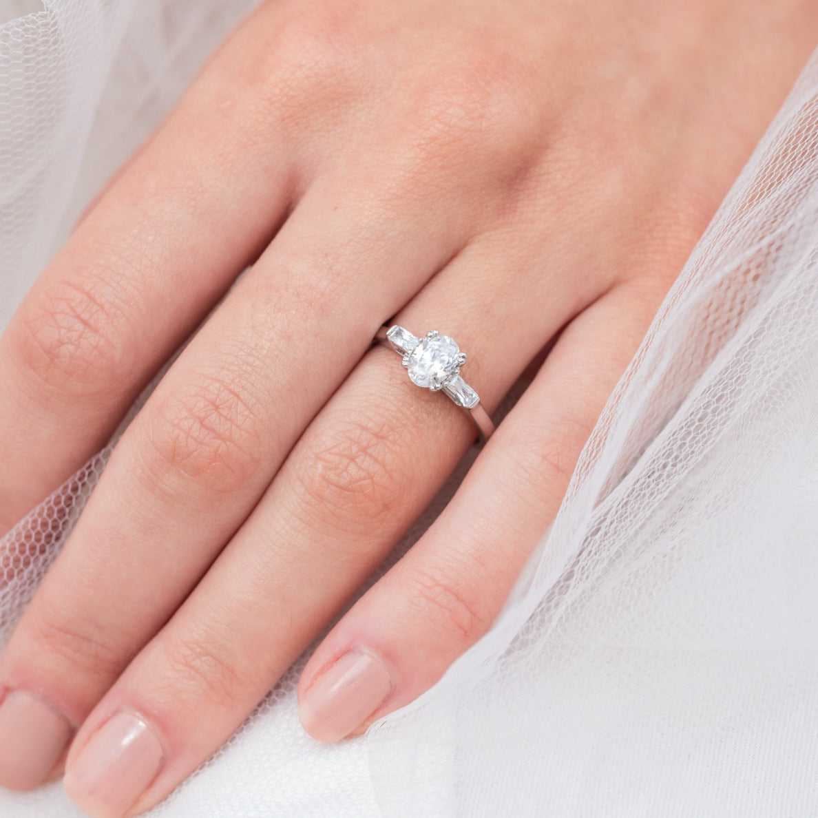 Audrey - Micheli Jewellery. engagement ring modelled on hand. oval diamond engagement ring. trilogy engagement ring. engagement ring with baguette side stones. white gold engagement ring. engagement ring on a hand model.