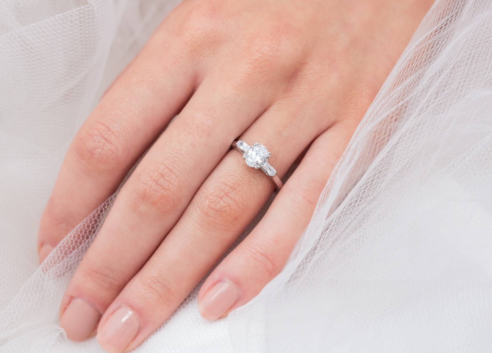 Audrey - Micheli Jewellery. engagement ring modelled on hand. oval diamond engagement ring. trilogy engagement ring. engagement ring with baguette side stones. white gold engagement ring. engagement ring on a hand model.